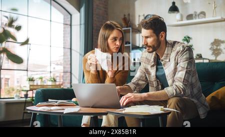 Contabilità a casa: Coppia con computer portatile, consulenza in appartamento. Young Family che compila moduli fiscali, documenti ipotecari, bollette, assegni, saldi, le fatture sono in ordine Foto Stock