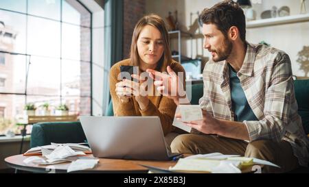 Stressante e drammatico contabilità a casa: Coppia con computer portatile e divano nell'appartamento. Young Family che compila moduli fiscali, documenti ipotecari, bollette, assegni, saldi, le fatture sono in ordine Foto Stock