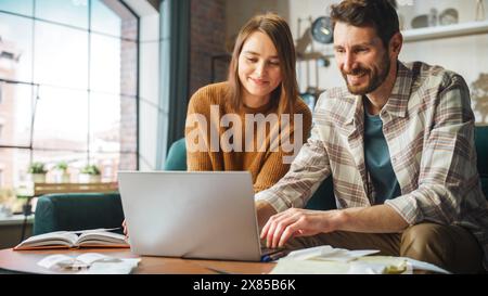 Fare contabilità a casa: Coppia felice che usa il computer portatile e si siede sul divano dell'appartamento. Young Family che compila moduli fiscali, documenti ipotecari, bollette, assegni, saldi, le fatture sono in ordine Foto Stock