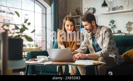 Contabilità a casa stressante: Coppia con computer portatile e divano nell'appartamento. Young Family che compila moduli fiscali, documenti ipotecari, bollette, assegni, saldi, le fatture sono in ordine Foto Stock