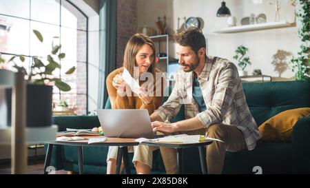 Contabilità a casa: Coppia con computer portatile, consulenza in appartamento. Young Family che compila moduli fiscali, documenti ipotecari, bollette, assegni, saldi, le fatture sono in ordine Foto Stock