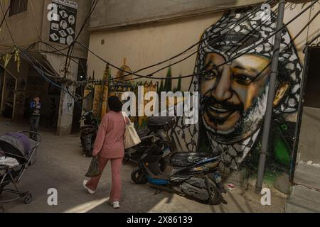 Beirut, Libano. 18 maggio 2024. Una donna cammina accanto a un murale raffigurante il defunto leader palestinese Yasser Arafat a Bourj el-Brajneh Refugee Camp, Beirut, Libano, il 18 maggio 2024. Circa 25.000 palestinesi vivono a Bourj el-Brajneh. (Foto di Collin Mayfield/Sipa USA) credito: SIPA USA/Alamy Live News Foto Stock