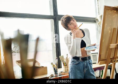 Donna dipinge creativamente su cavalletto, tenendo il pennello. Foto Stock