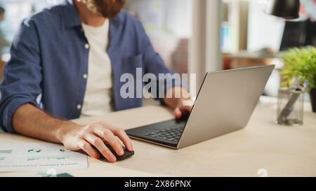 Primo piano Ritratto di un bellissimo manager con capelli lunghi seduto a una scrivania in Creative Office. Uomo elegante che utilizza un computer portatile in Marketing Company. Scrivere idee di Startup Business. Foto Stock
