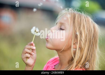 Primo piano di una bambina che soffia il dente di leone in un campo d'estate Foto Stock