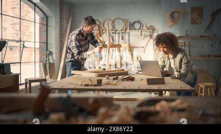 Proprietari di piccole imprese di un negozio di mobili che lavora su una nuova sedia da pranzo in legno. Carpentiere che costruisce la sedia, mentre Young Female Manager utilizza un computer portatile. Foto Stock