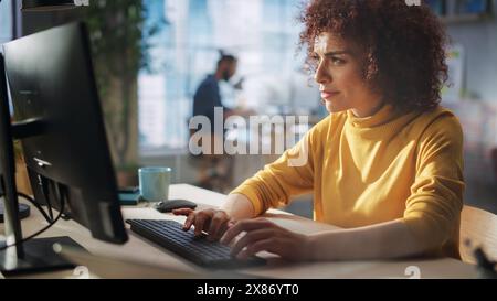Primo piano Ritratto di un felice responsabile del Medio Oriente che lavora in Creative Office. Giovane donna elegante con capelli ricci che usa il computer in Marketing Agency. Riprese cinematografiche attraverso una parete di vetro. Foto Stock