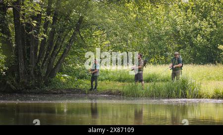 Tre pescatori si divertono a pescare circondati dalla natura lussureggiante della riva del fiume. Hobby e attività all'aperto. Foto Stock