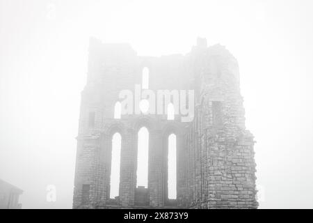 Una scena nebbiosa con le rovine di un antico edificio in pietra con alte finestre strette e archi. La struttura sembra essere parzialmente compressa, Foto Stock