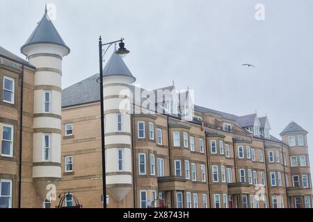 Una fila di moderni edifici in mattoni con torri cilindriche uniche e tetti conici. Gli edifici hanno finestre multiple e si trovano sotto una nuvolosa Foto Stock