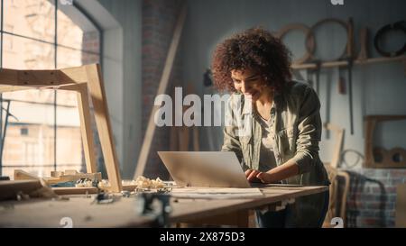 Primo piano Ritratto di un artista multietnico che utilizza un computer portatile. Black Creative Female digitando e-mail, navigando in Internet, creando un progetto online in uno studio di loft con strumenti a muro. Foto Stock