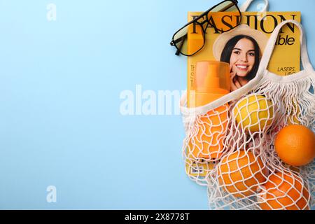 Borsa a cordoncino con caricatore, frutta e accessori estivi su sfondo azzurro, piatto. Spazio per il testo Foto Stock