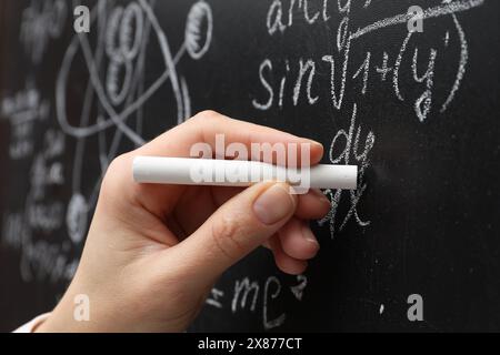 Insegnante che scrive formule matematiche con gesso sulla lavagna, primo piano Foto Stock