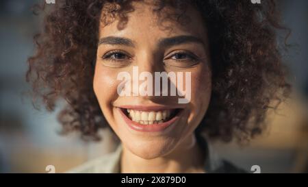 Primo piano Ritratto di una bellissima donna creativa con capelli ricci sorridenti. Giovane donna araba multietnica di successo che lavora in Art Studio. Sognando una vita migliore e opportunità per il futuro. Foto Stock