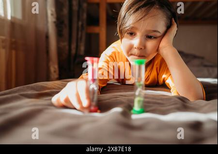 Un ragazzo carino e premuroso che guarda la clessidra a letto a casa Foto Stock