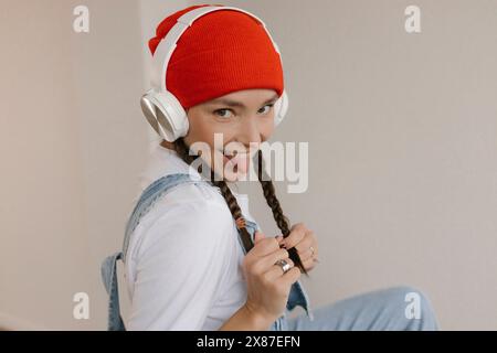 Donna giocosa che si alza la lingua ascoltando la musica tramite le cuffie wireless Foto Stock