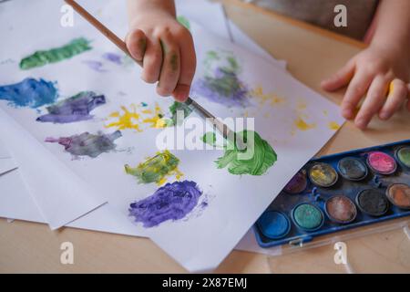 Ragazzo che fa tratti di colore su carta con la spazzola a casa Foto Stock
