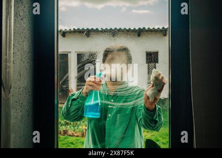 Uomo che pulisce la finestra con una soluzione di sapone Foto Stock