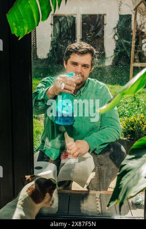 Uomo che spruzza sapone liquido su una finestra di vetro Foto Stock