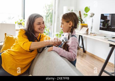 Nonna felice che ascolta il battito cardiaco della nipote attraverso lo stetoscopio a casa Foto Stock