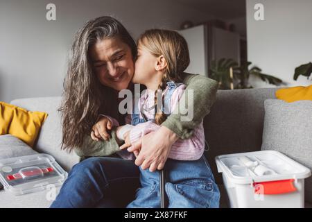 Nipote che bacia la nonna felice seduta sul divano di casa Foto Stock