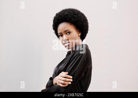 Donna afro che indossa una camicia nera davanti al muro bianco Foto Stock