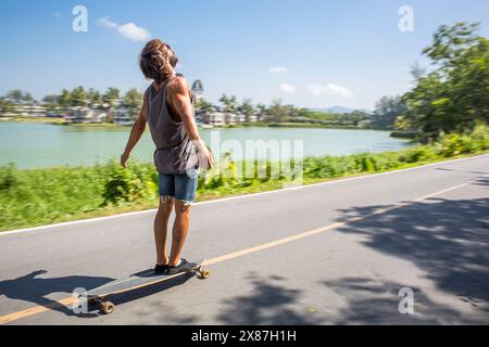 Uomo in piedi sullo skateboard in movimento vicino al lago Foto Stock