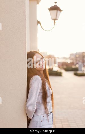 Sorridente giovane donna appoggiata al muro dell'edificio Foto Stock