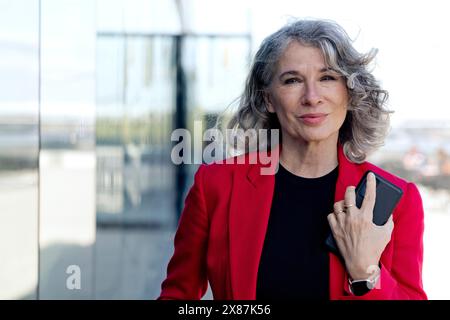 Donna d'affari sorridente e anziana con smartphone in mano Foto Stock