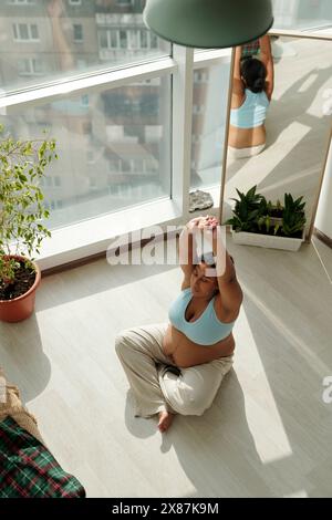 Donna incinta con le braccia sollevate facendo esercizio di riscaldamento alla finestra a casa Foto Stock
