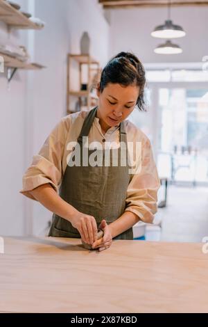 Artista esperto che formava l'argilla in piedi accanto a un tavolo sul posto di lavoro in ceramica Foto Stock