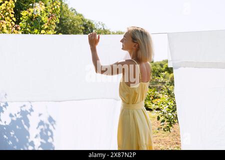 Donna bionda che appende lenzuola bianche su una linea di stoffa nel cortile posteriore Foto Stock