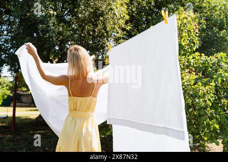 Donna bionda che appende lenzuola bianche nel cortile posteriore Foto Stock