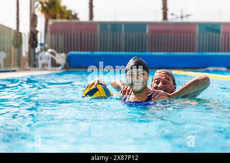 Giocoso uomo anziano e giovane donna che si divertono insieme in piscina Foto Stock