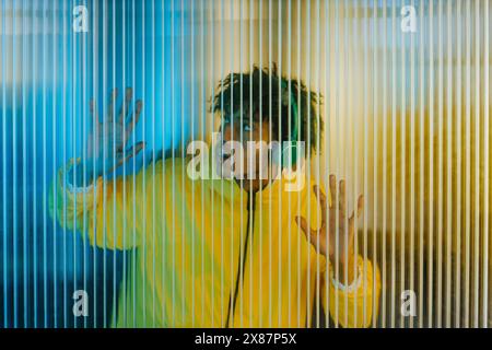 Giovane uomo che indossa le cuffie e ascolta musica vicino a una parete a righe Foto Stock