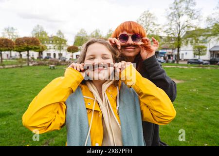 Mamma e figlia sorridenti che fanno i baffi con i capelli al parco Foto Stock