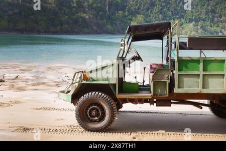 Vista laterale di un vecchio parcheggio vintage AIL Abir sulla sabbia in riva al mare, nostalgia in stile retrò, stampe di pneumatici sulla spiaggia sabbiosa con acqua verde e fores Foto Stock