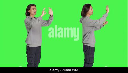 Giovane modella che mostra il simbolo "OK" in studio, che agisce contento e contento con qualcosa sullo sfondo verde. L'uomo asiatico si sente positivo e mostra accordo o dà la sua approvazione. Foto Stock
