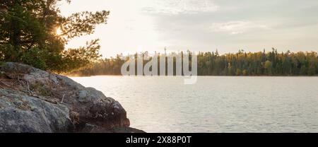 Alba dietro rocce e pini su un lago di confine durante l'autunno Foto Stock