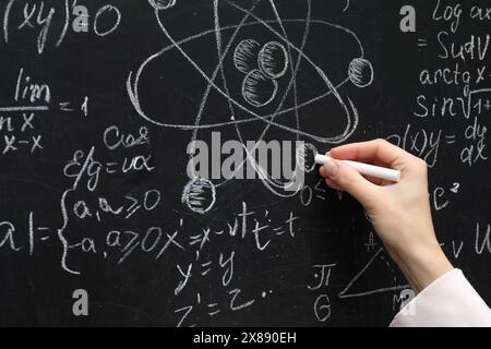 Insegnante che scrive formule fisiche con gesso su lavagna nera, primo piano Foto Stock