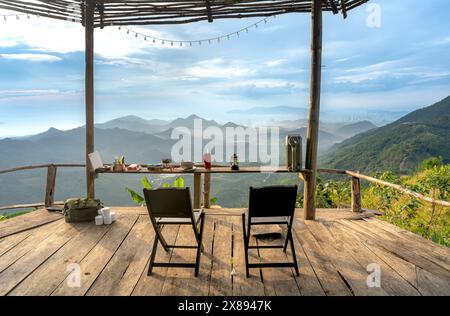 Sulla cima della montagna nel comune di DAC Loc, Nha Trang, Vietnam - 17 maggio 2024: Tavoli e sedie in legno con vista sull'alba sull'alta montagna Foto Stock