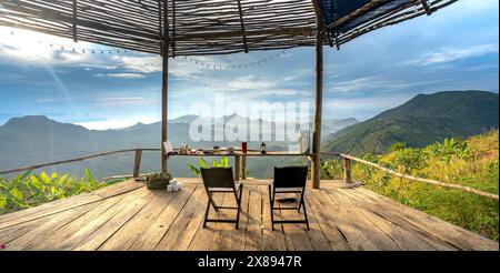 Sulla cima della montagna nel comune di DAC Loc, Nha Trang, Vietnam - 17 maggio 2024: Tavoli e sedie in legno con vista sull'alba sull'alta montagna Foto Stock