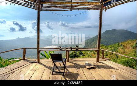 Sulla cima della montagna nel comune di DAC Loc, Nha Trang, Vietnam - 17 maggio 2024: Tavoli e sedie in legno con vista sull'alba sull'alta montagna Foto Stock