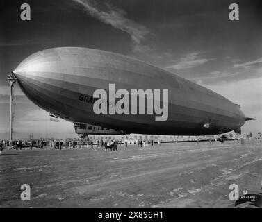 Vista laterale anteriore di tre quarti del dirigibile Graf Zeppelin seduto a terra e legato mentre un gruppo di persone osserva. Foto Stock