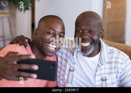 Padre afroamericano anziano e figlio adulto a casa, a fare selfie Foto Stock