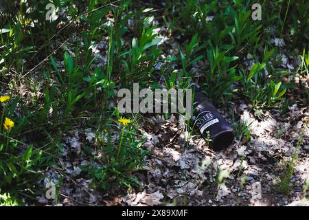 Una bottiglia di profumo è stesa a terra in una zona erbosa. La bottiglia è nera e ha un'etichetta. La scena è tranquilla e serena Foto Stock