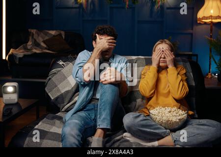 Uomo e donna sono seduti su un divano che copre gli occhi con le mani Foto Stock