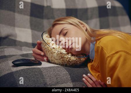 Una donna addormentata sta riposando tenendo la testa nel piatto con popcorn Foto Stock