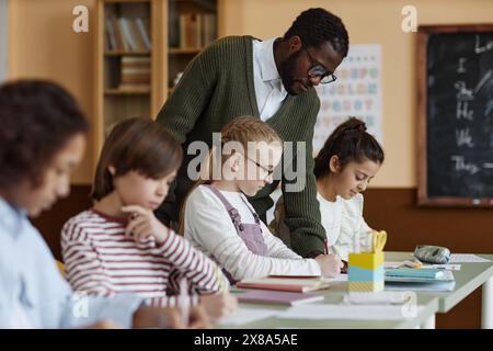 Insegnante afroamericano di inglese che lavora in classe guardando i bambini che fanno esercizio di scrittura Foto Stock