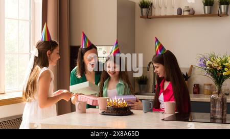 La famiglia si riunisce in giro mentre una ragazza apre i suoi regali di compleanno, sorridendo ed eccitata. Essenza ed emozioni delle celebrazioni di compleanno, atmosfera di gioia a Foto Stock